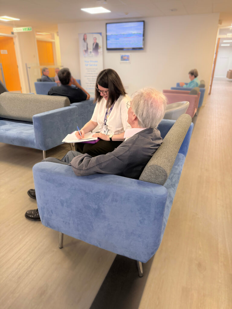 Shows 2 people talking on a sofa in a waiting/lounge area.