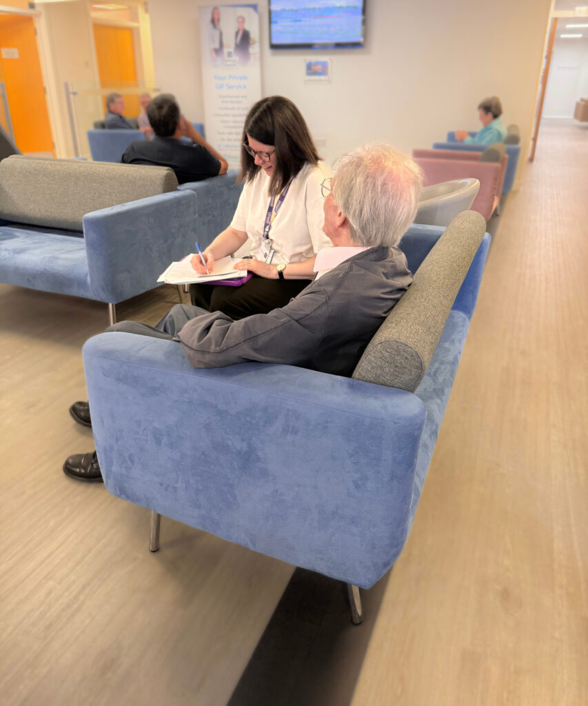 Shows 2 people talking on a sofa in a waiting/lounge area.