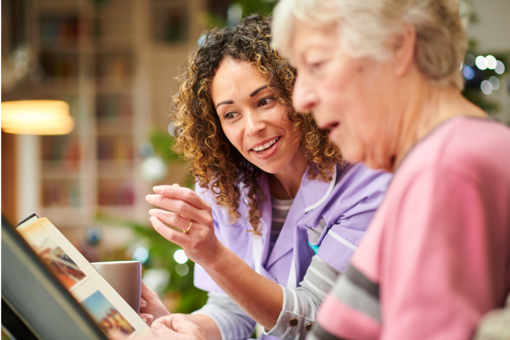 Photo shows someone looking at a photogrpah album with an older person.