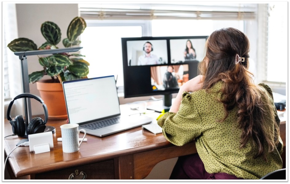Person is sat at a desk, facing away from the camera. They are looking at their laptop, which is showing an online meeting.